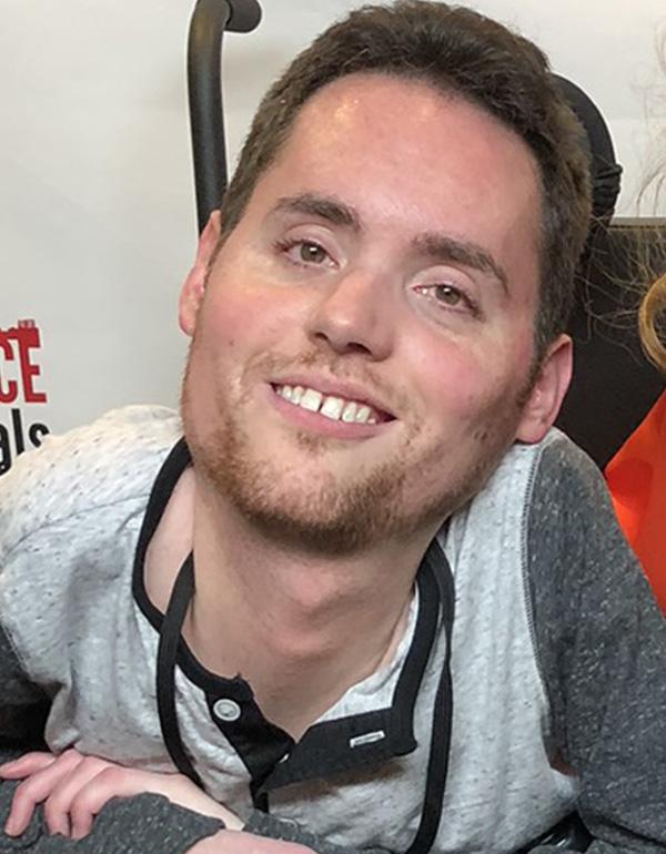 A mid 30s man in a wheelchair smiling at the camera.