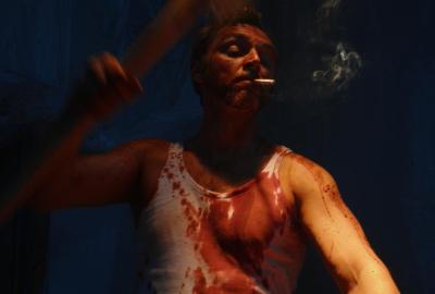 A bloodied man smoking a cigarette while he beats someone