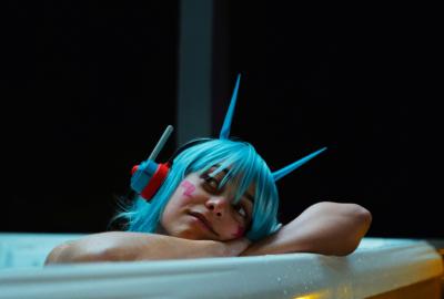 Poppy with blue hair and headphones looks up from the bathtub