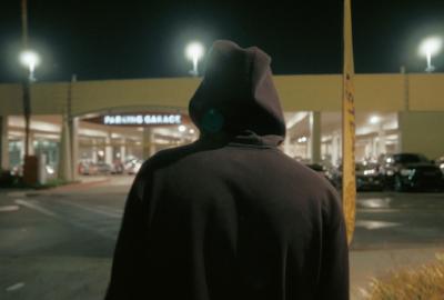 Man in hoodie looks at a store from the parking lot