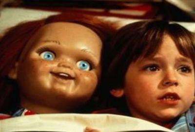 Child's Play film still boy lays in bed with Chucky doll