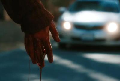 A bloody hand drips blood on the road as a car approaches