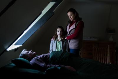 Home Education film still mother, daughter looking over father in bed