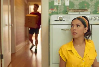 Movin Day film still woman sitting in kitchen as boyfriend brings in a moving box