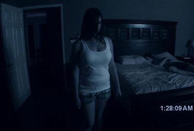 Paranormal Activity woman stands in a dark bedroom